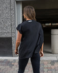 A woman wearing a black asymmetrical t-shirt and a pair of black organic cotton leggings by Malaika New York
