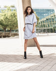 A woman wearing a grey knee-lenght shift dress with a belt by Malaika New York