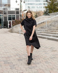 A woman walking wearing a knee length black shift dress by Malaika New York
