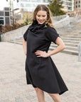A woman wearing a knee length black shift dress by Malaika New York
