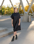 A front view of a woman wearing a pleated black shift dress by Malaika New York