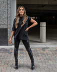 A woman wearing an asymmetrical black t-shirt in organic cotton and a pair of faux leather leggings by Malaika New York