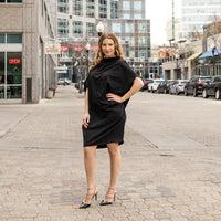 a woman wearing a black knee length shift dress by malaika new york