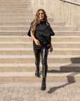 A blond woman wearing an oversize organic cotton black t-shirt & faux leather leggings