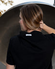 A woman with her back turned to show the label on her black boat neck t-shirt by Malaika New York