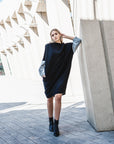 A woman standing with her hand in a pocket on her black long sleeve dress by Malaika New York