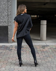 A woman showing the back of her beautiful asymmetrical organic cotton top and vegan leather leggings by Malaika New York