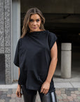 A close up of a woman wearing an asymmetrical black organic cotton t-shirt and a pair of faux leather leggings by Malaika New York