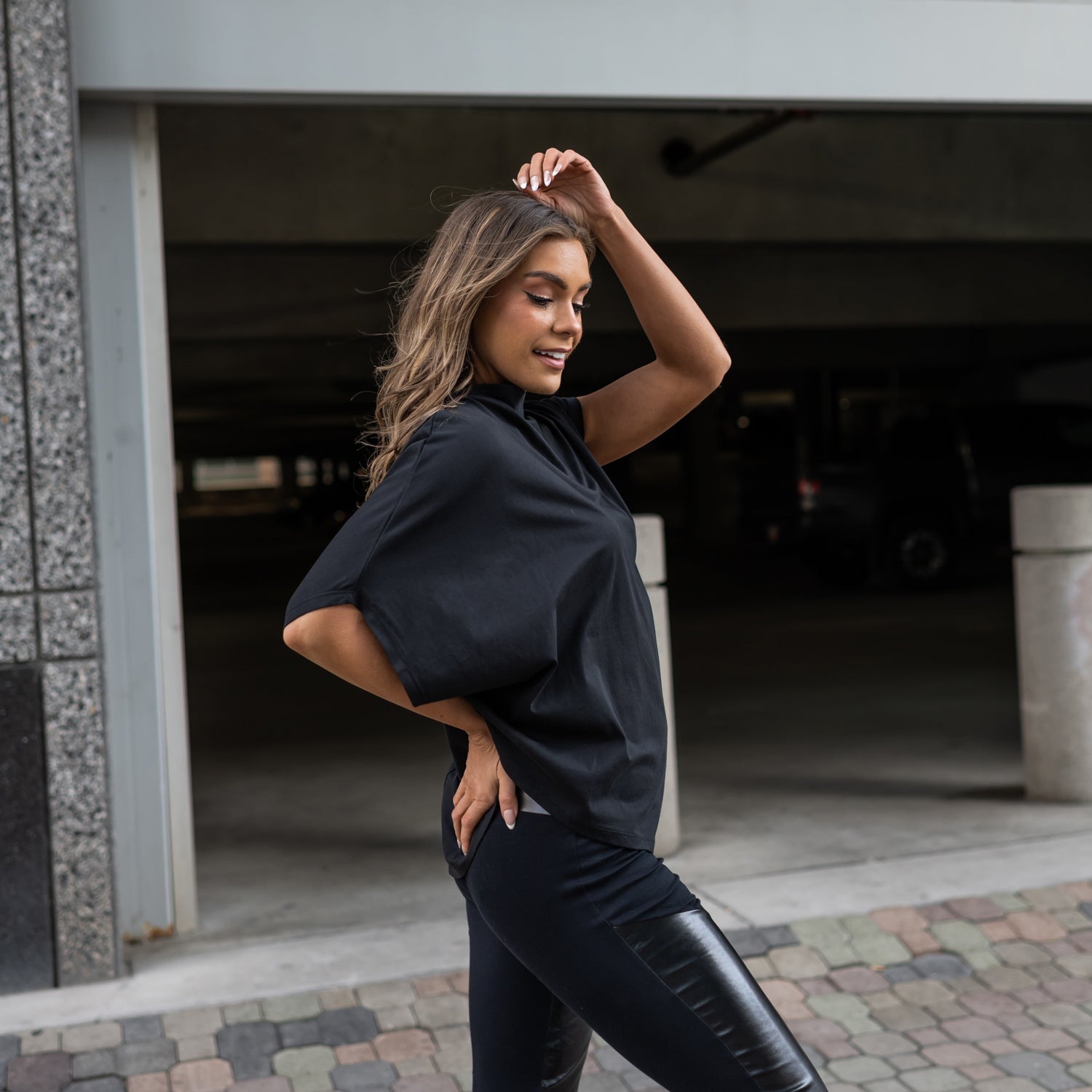 A side view of a woman wearing our vegan leather leggings with organic cotton on the back and front with an asymmetrical t-shirt by Malaika New York