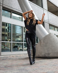 A woman wearing a pair of shiney & matte vegan leather leggings and a black asymmetrical top by Malaika New York