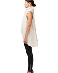 A woman standing with her side turned wearing a white faux fur asymmetrical vest with black snaps & a pair of black organic cotton leggings by Malaika New York