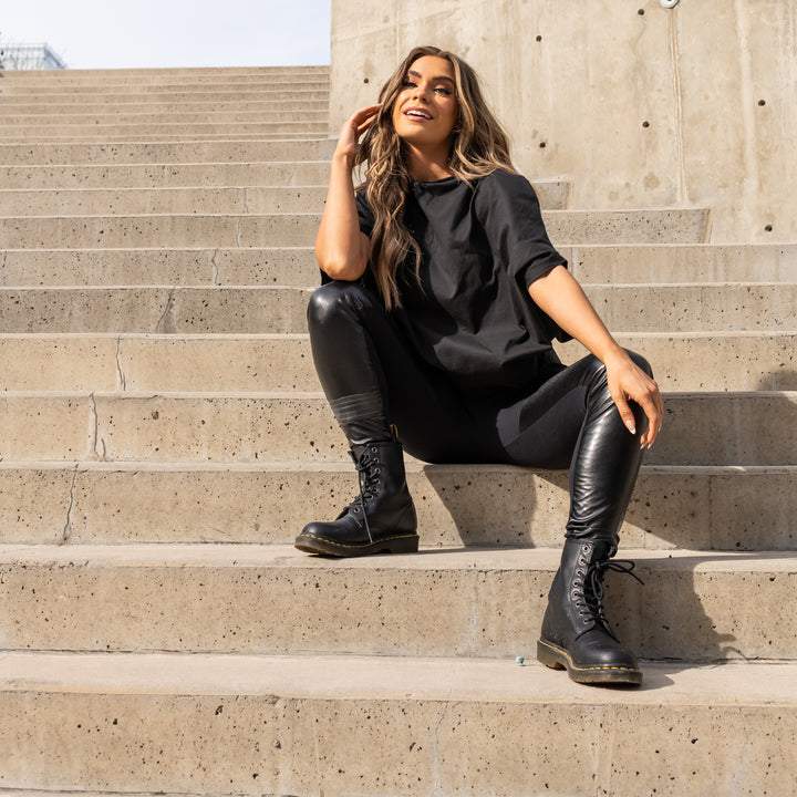 A woman sitting a flight of stairs wearing a pair of black vegan leather leggings & an organic cotton oversized t-shirt by Malaika New York