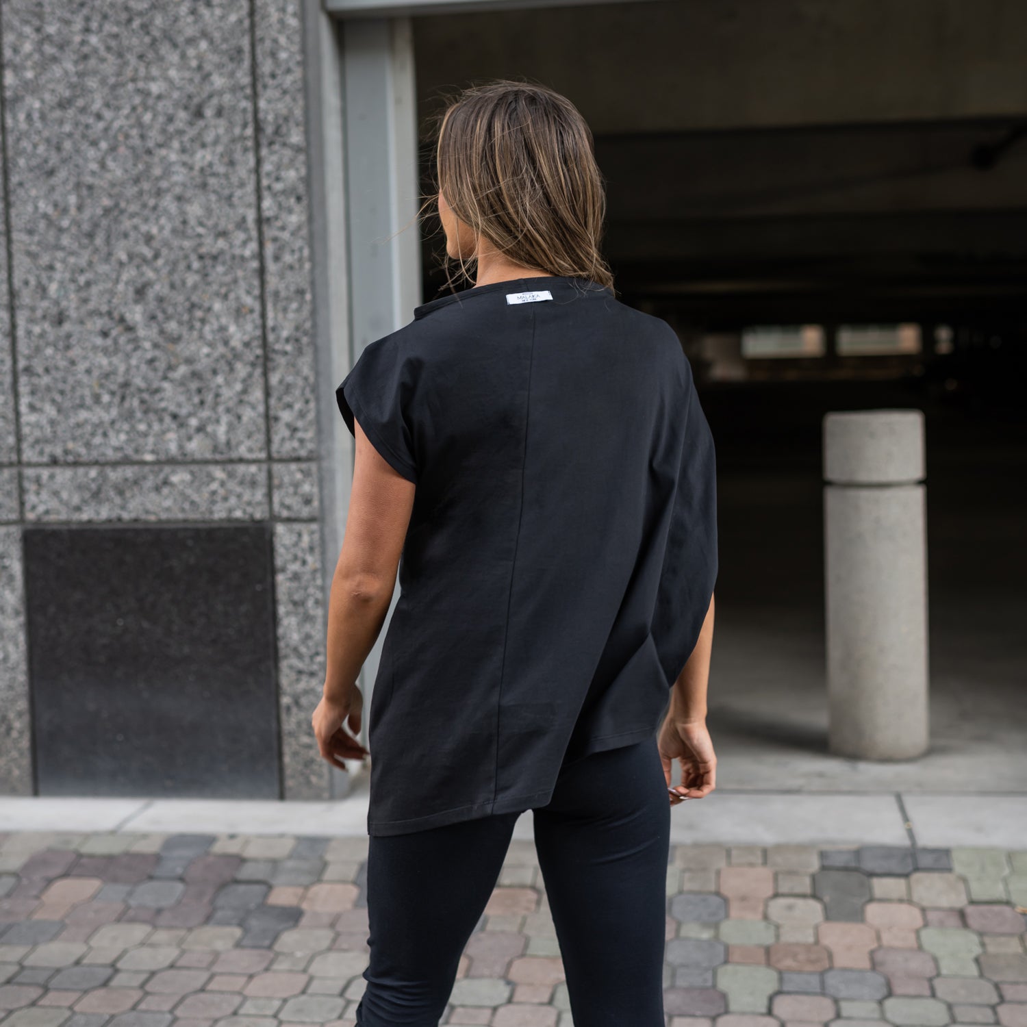 A woman wearing a black asymmetrical t-shirt and a pair of black organic cotton leggings by Malaika New York