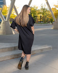 A back view of a woman wearing a pleated black shift dress by Maaika New York