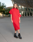 A woman wearing a pleated knee-lenght red dress by Malaika New York
