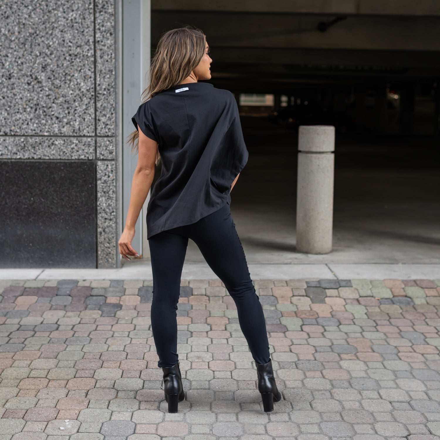 A back view of a woman wearing a black asymmetrical t-shirt by Malaika New York
