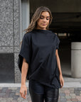 A woman wearing a black on black look by Malaika New York. A pair of faux leather leggings paired with an asymmetrical t-shirt
