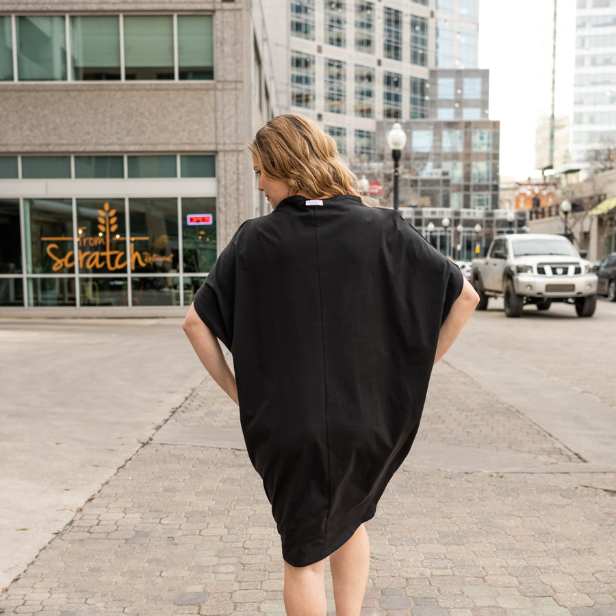 a woman walking away from the camera wearing a black shift dress by malaika new york