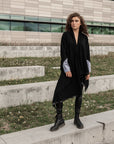A woman wearing a black waterfall cardigan paired with dr. martens boots and a pair of faux leather leggings by Malaika New York