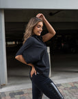 A woman wearing a black asymmetrical t-shirt with a pair of faux leather leggings by Malaika New York