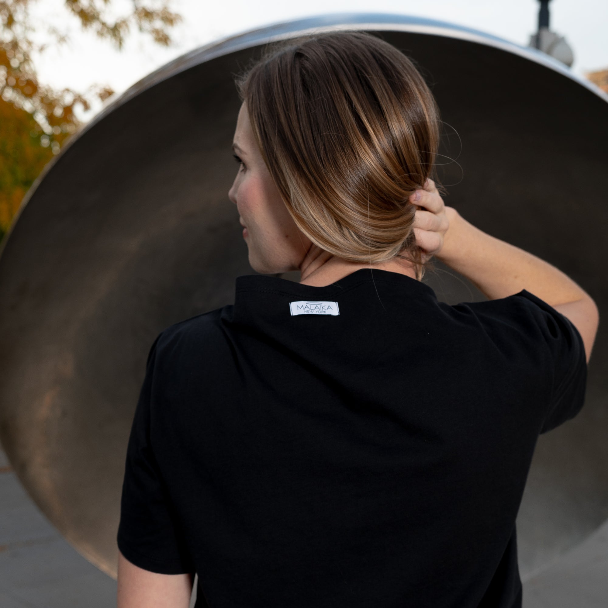 A woman with her back turned to show the label on her black boat neck t-shirt by Malaika New York