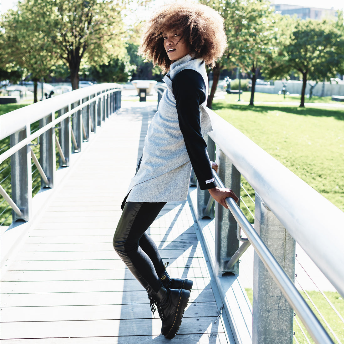 A woman wearing wearing a grey cardigan with black sleeves and a pair of faux leather leggings by Malaika New York