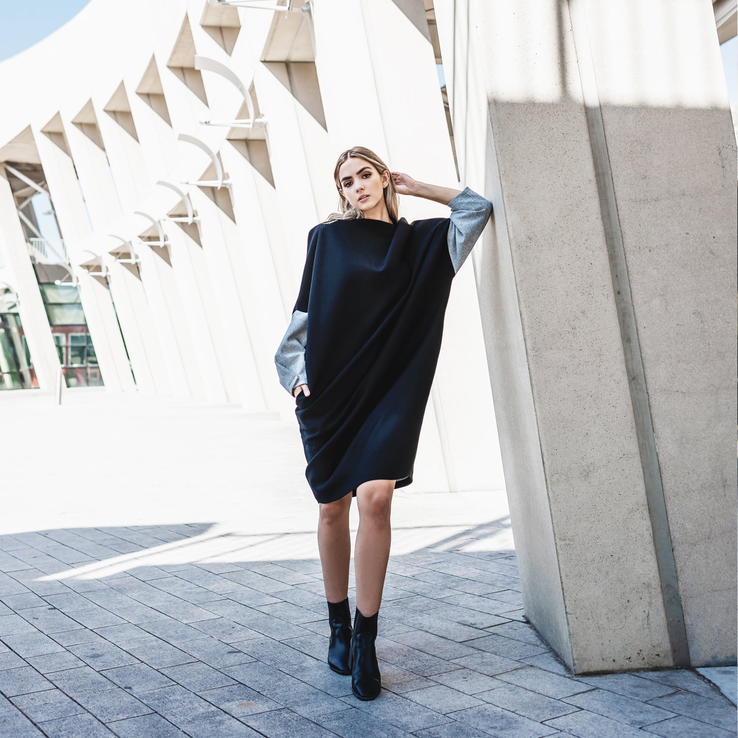 A woman standing with her hand in a pocket on her black long sleeve dress by Malaika New York