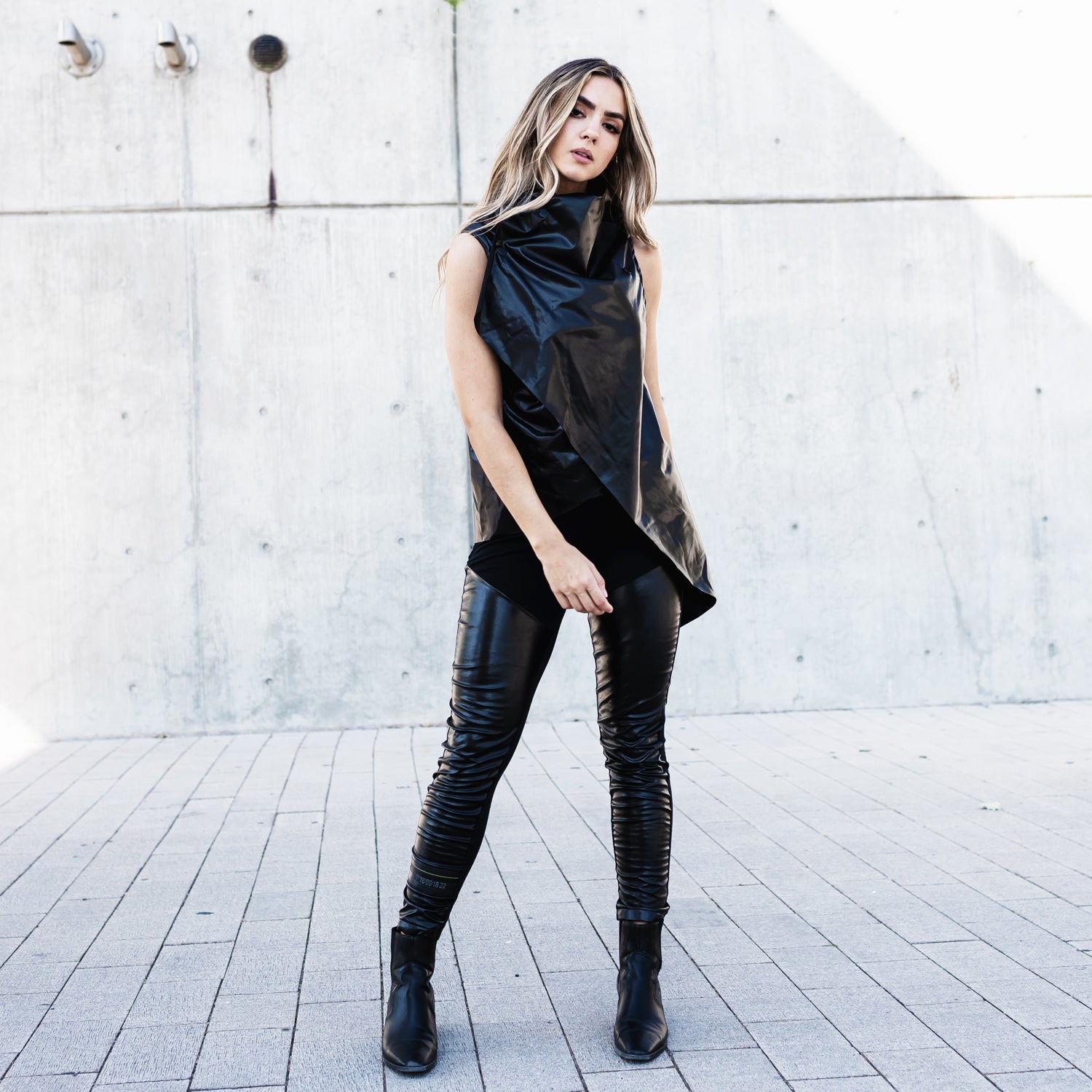 A woman wearing a vegan faux leather asymmetrical vest &amp; a pair of vegan leather leggings by Malaika New York