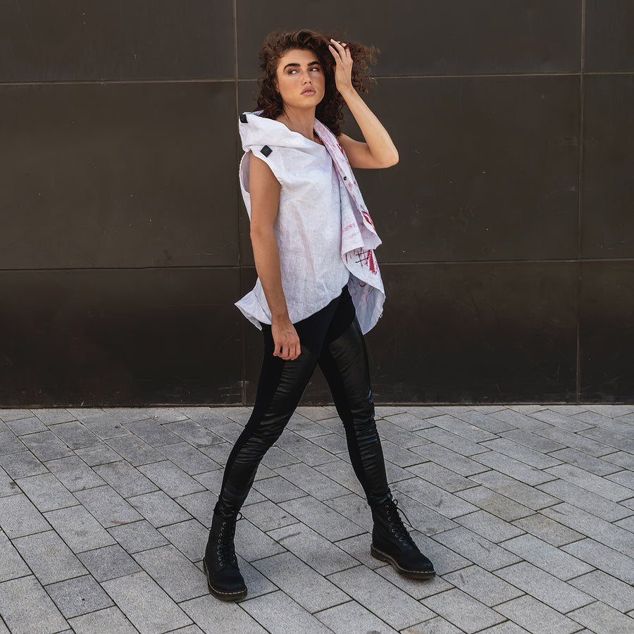 A woman wearing a white linen summer vest and faux leather leggings by Malaika New York