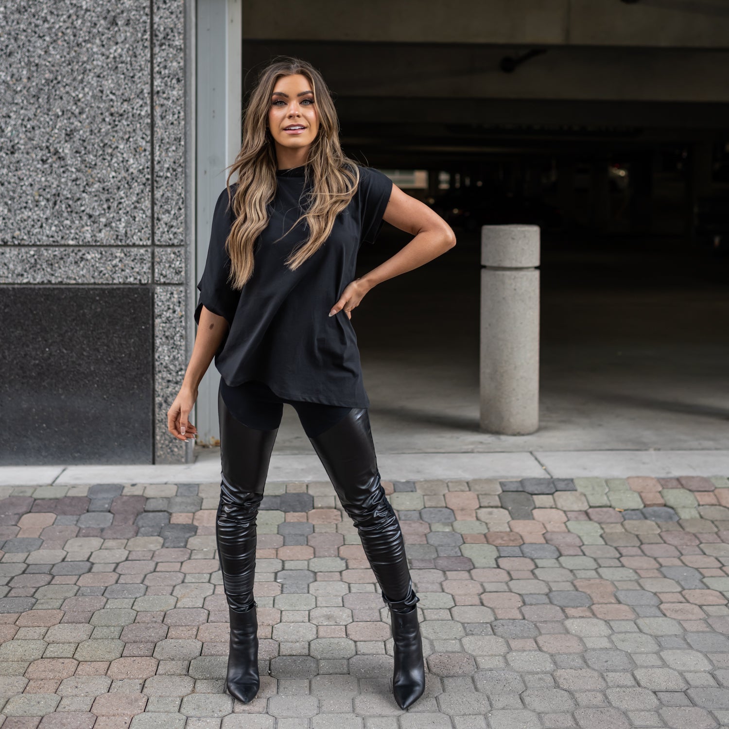 A woman wearing a pair of vegan black leather leggings mixed with organic cotton. She is also wearing a black asymmetrical top by Malaika New York