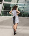A woman wearing a beautiful grey wrap dress in organic cotton. The model is showing the back of the dress where she has formed a beautiful bow with the long black tie by Malaika New York
