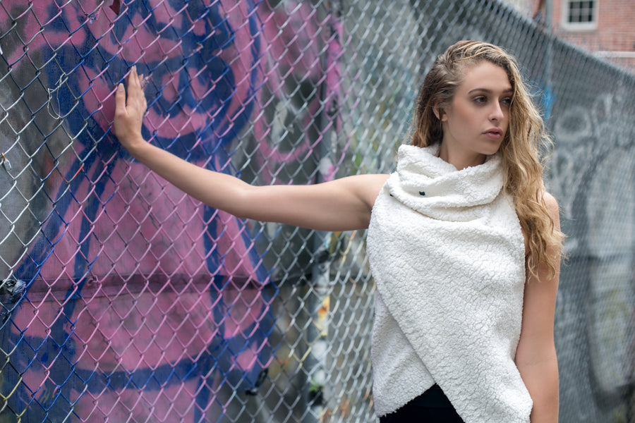 A woman wearing a white faux fur asymmetrical vest with black snaps & a pair of black organic cotton leggings by Malaika New York